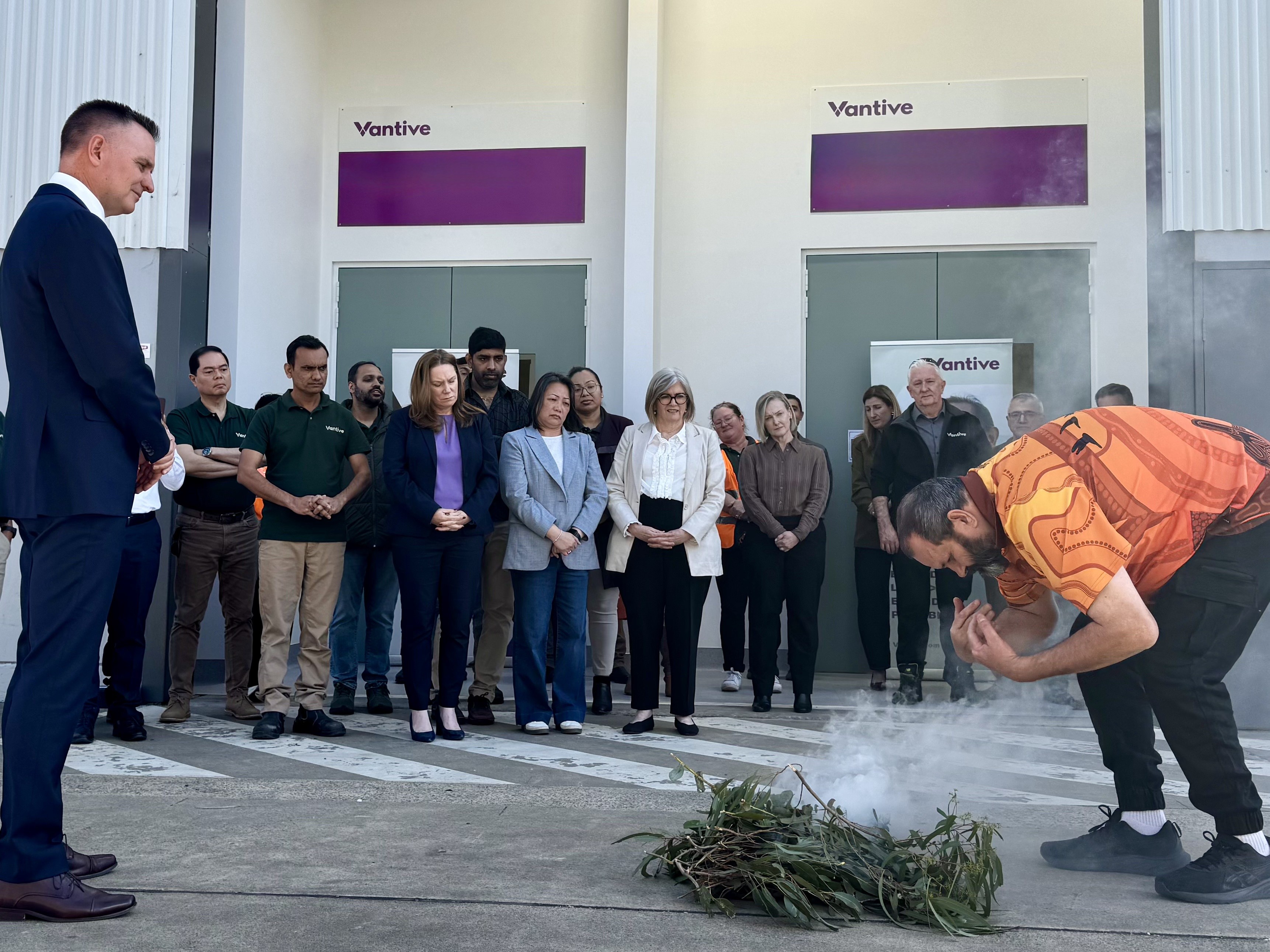 Group gathered outside the Vantive Central Service Hub during a smoking ceremony, with a participant performing the ceremony in the foreground.
