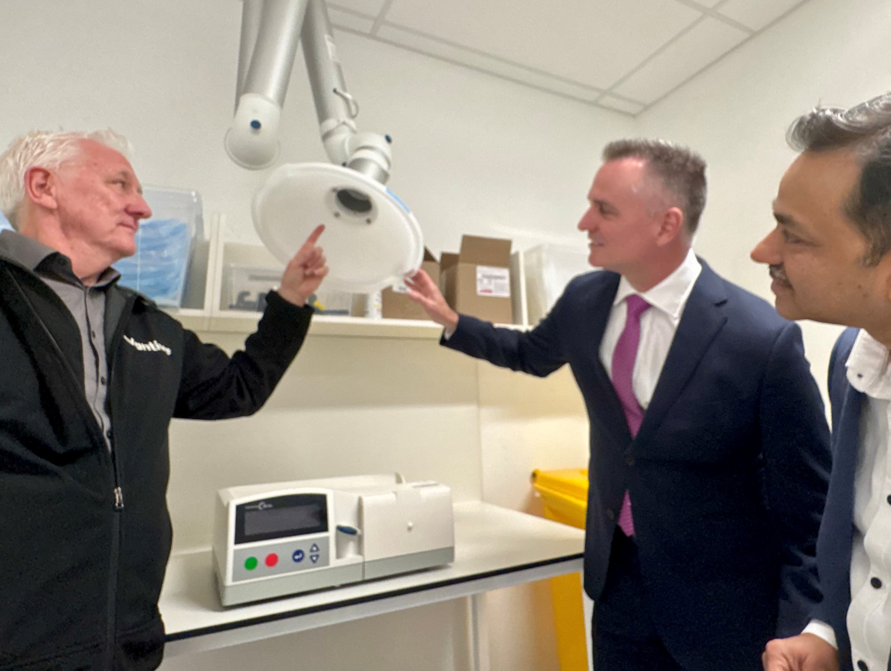 Three people touring a clinical equipment area and examining equipment inside the Central Service Hub.