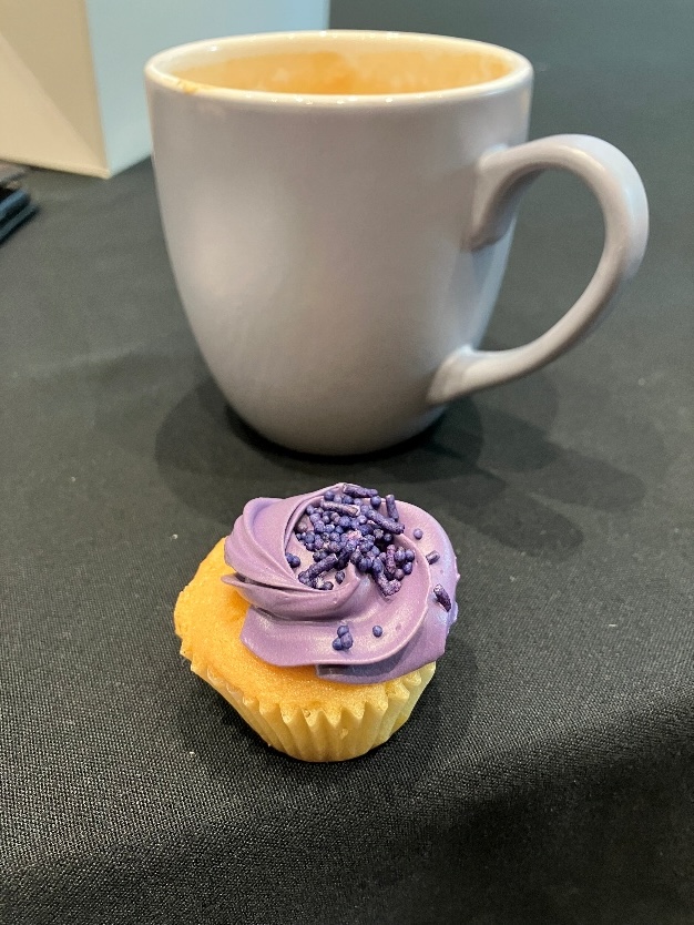 Cupcake with purple frosting beside a coffee cup at a conference table.