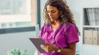 A woman in scrubs holding a tablet in an office environment