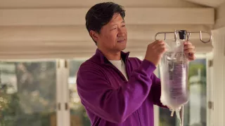 A man in his living room hangs up his bag of Dianeal peritoneal dialysis (PD) solution