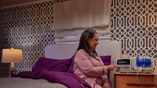 Patient sits on her bed and interacts with the Homechoice Claria system on her nightstand