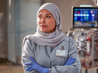 A healthcare professional stands with arms crossed looking into the distance, in front of the PrisMax System