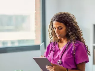 Healthare professional in scrubs looks at their tablet 