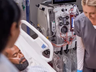 Healthcare professional at the patient bedside in front of the PrisMax System