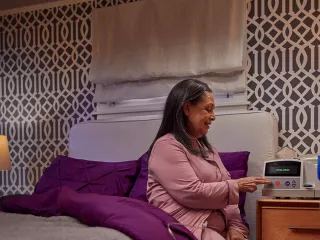 Patient sits on her bed and interacts with the Homechoice Claria system on her nightstand